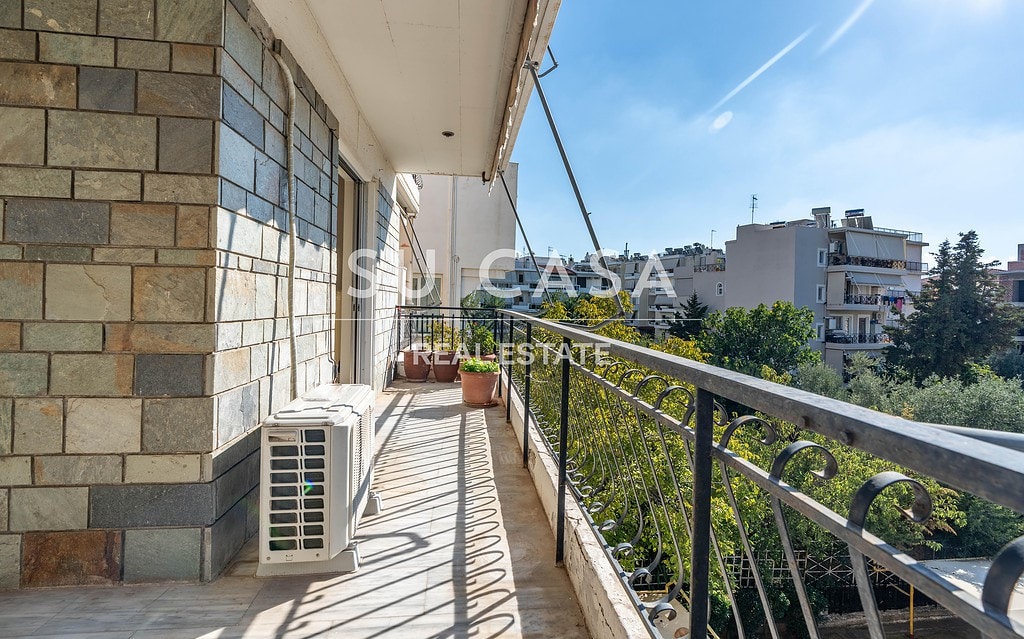Εξωτερική βεράντα διαμερίσματος στην Αθήνα με πράσινο και εντυπωσιακή θέα σε πολυκατοικίες και ουρανό.