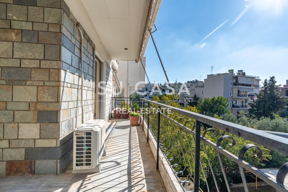 Εξωτερική βεράντα διαμερίσματος στην Αθήνα με πράσινο και εντυπωσιακή θέα σε πολυκατοικίες και ουρανό.