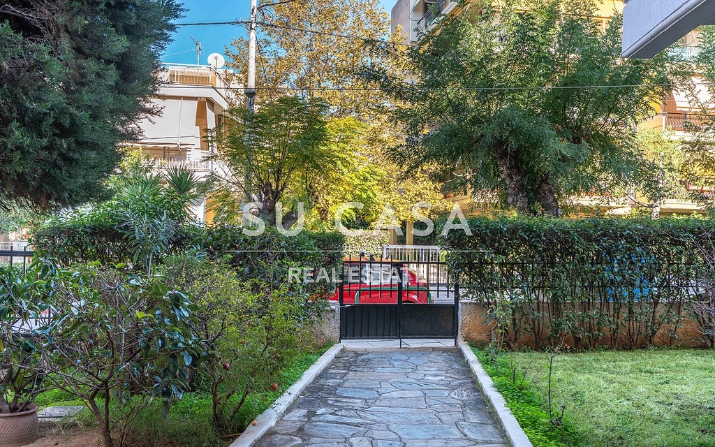 Πράσινος κήπος με δέντρα και διαδρομή με πέτρα, ηρεμία και φύση κοντά σε κατοικίες.