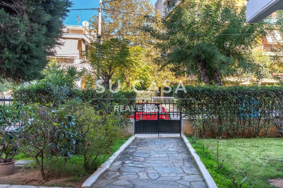 Πράσινος κήπος με δέντρα και διαδρομή με πέτρα, ηρεμία και φύση κοντά σε κατοικίες.