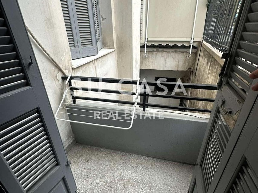 Μικρό μπαλκόνι διαμερίσματος με σιδερένια ράφια και κάγκελα, ιδανικό για αποθήκευση ή χαλάρωση.