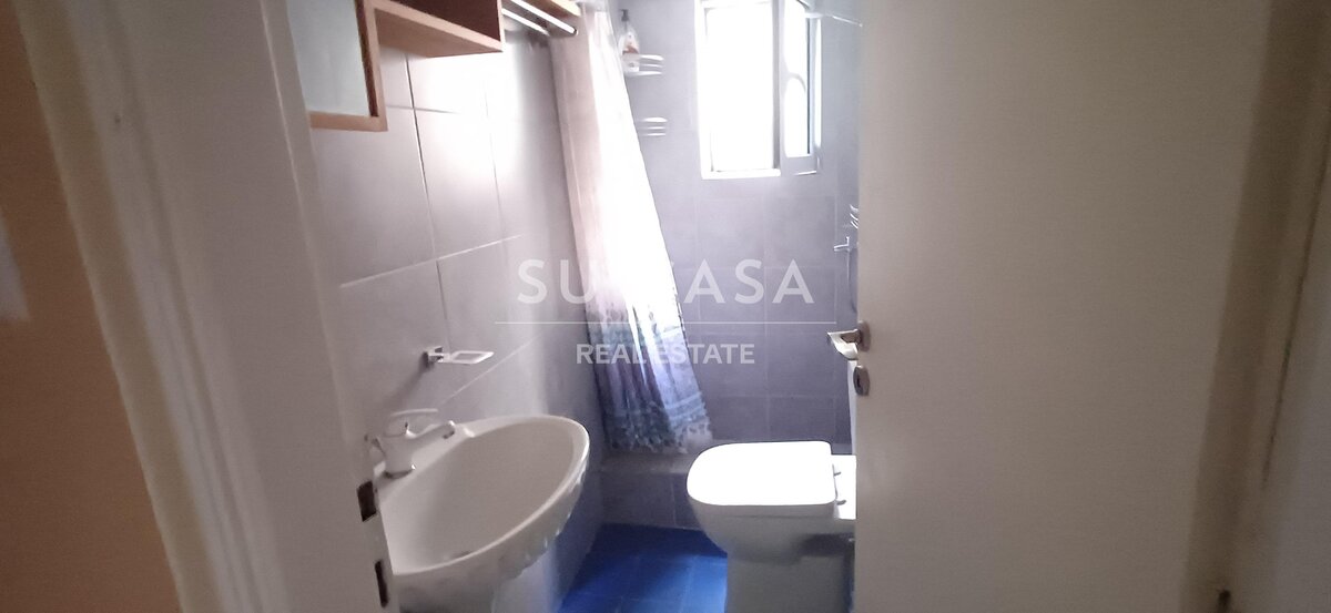 Μικρό μπάνιο με λευκά πλακάκια, νιπτήρα και παράθυρο, σε διαμέρισμα στην Ελλάδα.