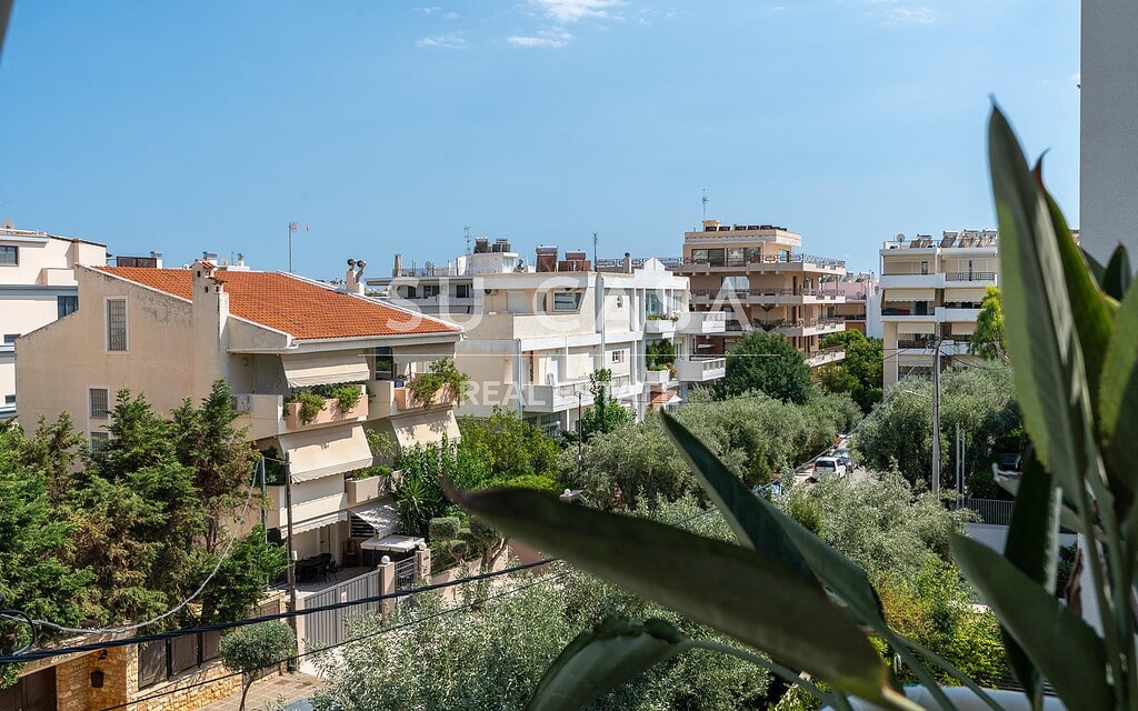 Θέα από διαμέρισμα στην Αθήνα με πράσινα δέντρα και πολυκατοικίες.