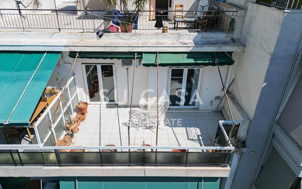 Μπαλκόνι διαμερίσματος με πράσινη σκιά και έπιπλα.
