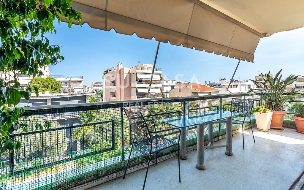 Μπαλκόνι με τραπέζι και καρέκλες, θέα σε πολυκατοικίες και πράσινο.