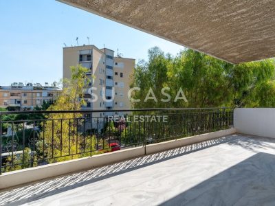 Ευρύ μπαλκόνι με θέα σε δέντρα και πολυκατοικίες, ιδανικό για χαλάρωση.
