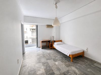 Εσωτερική εικόνα γκαρσονιέρας με μονό κρεβάτι και μπαλκόνι.